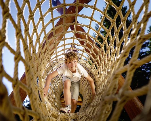 Abenteuerspielplatz Ein kleiner Junge klettert im Niederseilgarten des Familienhotels in Tirol
