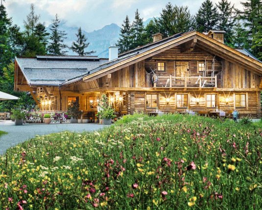 Außenansicht der Interalpen-Alm mit einer schönen Blumenwiese im Vordergrund