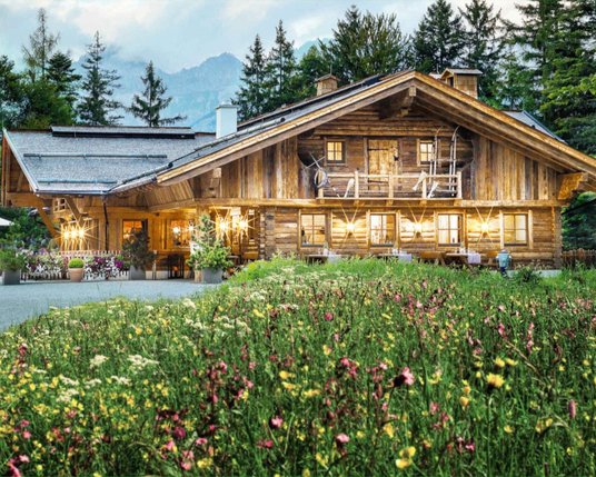 Außenansicht der Interalpen-Alm mit einer schönen Blumenwiese im Vordergrund