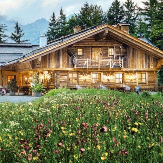 Interalpen-Alm und weitere Locations entdecken Außenansicht der Interalpen-Alm mit einer schönen Blumenwiese im Vordergrund