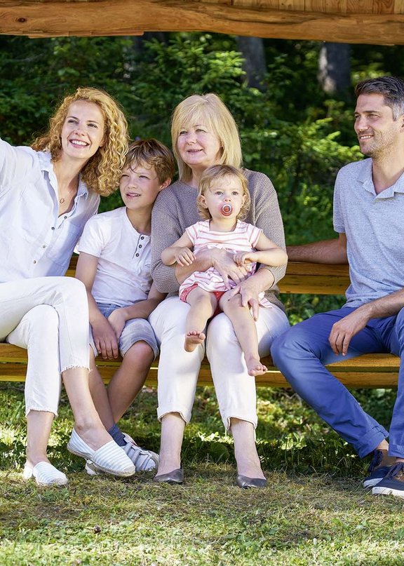Eine Familie mit ihren Kindern sitzt auf einer Bank in der wunderschönen Umgebung eines Familienhotels bei Seefeld