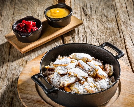 Nahaufnahme von hausgemachtem Kaiserschmarrn mit Preiselbeeren und Apfelmus in einem Eisengusstopf