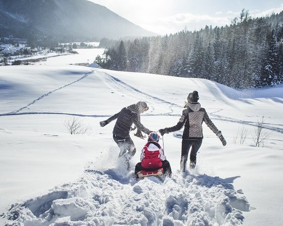 © Region Seefeld, Stephan Elsler Familie beim Rodeln in der verschneiten Tiroler Bergwelt